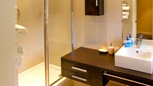 A bathroom with a glass shower enclosure, a dark vanity with a white sink, and a mirror above the sink. - Howle Hideaway (Ross-on-Wye)