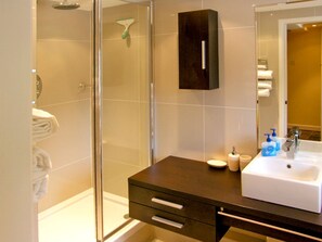 Ein Badezimmer mit Duschkabine aus Glas, einem dunklen Waschtisch mit weißem Becken und einem Spiegel darüber.