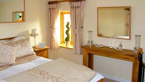 A bedroom with a bed, bedside tables, a dresser, a mirror, and a window with curtains. - Howle Hideaway (Ross-on-Wye)
