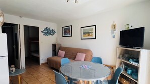 Een woonkamer met een ronde tafel, blauwe stoelen, een bruine bank, een televisie en een kast met servies.