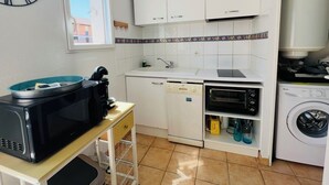 Een compacte keuken met witte kastjes, een magnetron, een oven, een vaatwasser en een wasmachine.