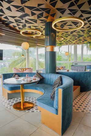 Ein modernes Interieur mit einem gewölbten blauen Sofa, einem runden Glastisch und einem geometrischen Deckendesign.