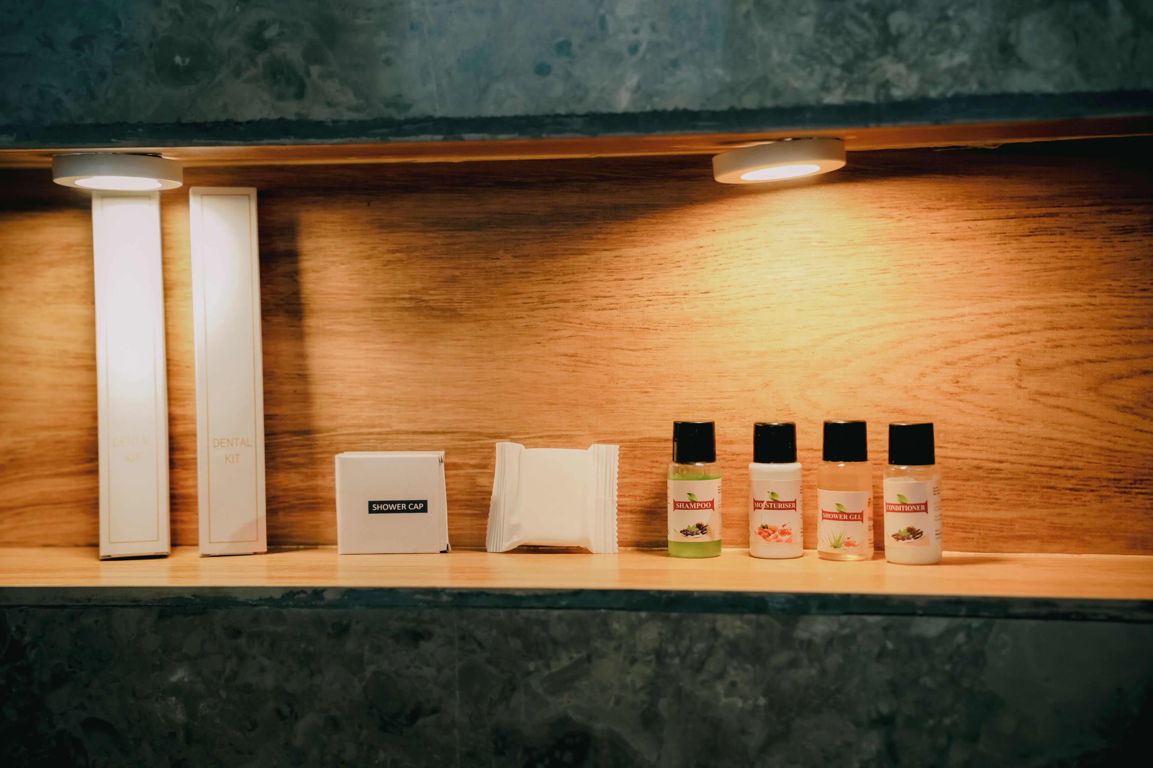 A shelf with a dental kit, a shower cap, and three bottles of toiletries.