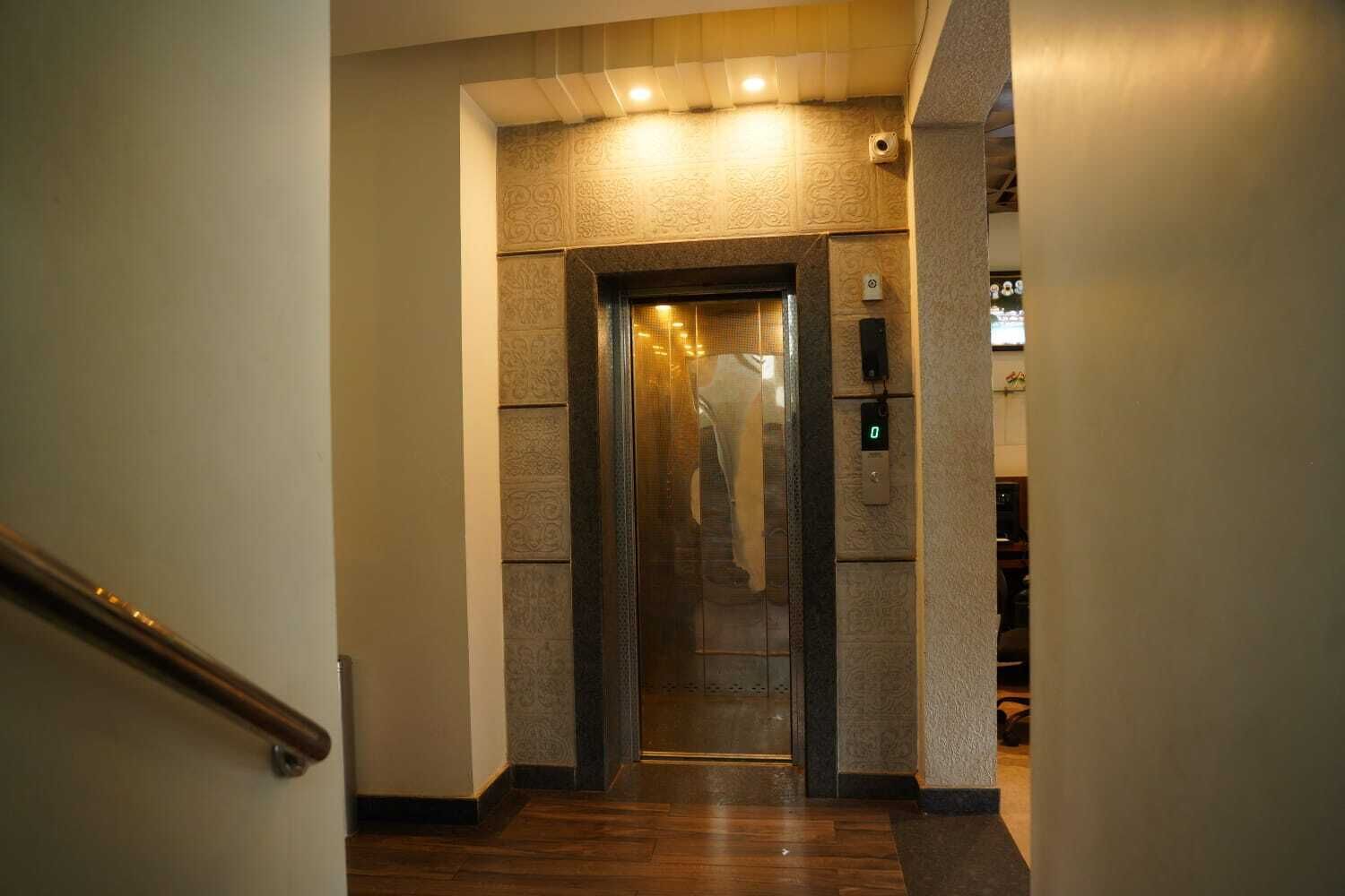 A hallway leading to an elevator with a wooden floor and patterned walls.