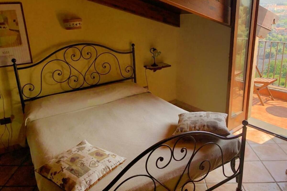 Una cama con cabecera de metal, una mesita de noche y una ventana con vistas al exterior.