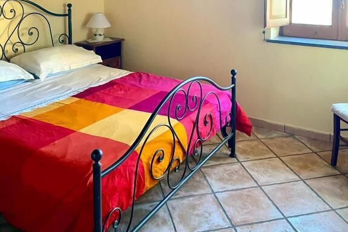 Un dormitorio con cama, vigas de madera en el techo, una ventana y una mesita de noche.