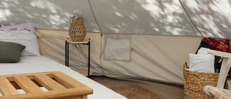 A tent with a bed, a small table, a lamp, and a basket.