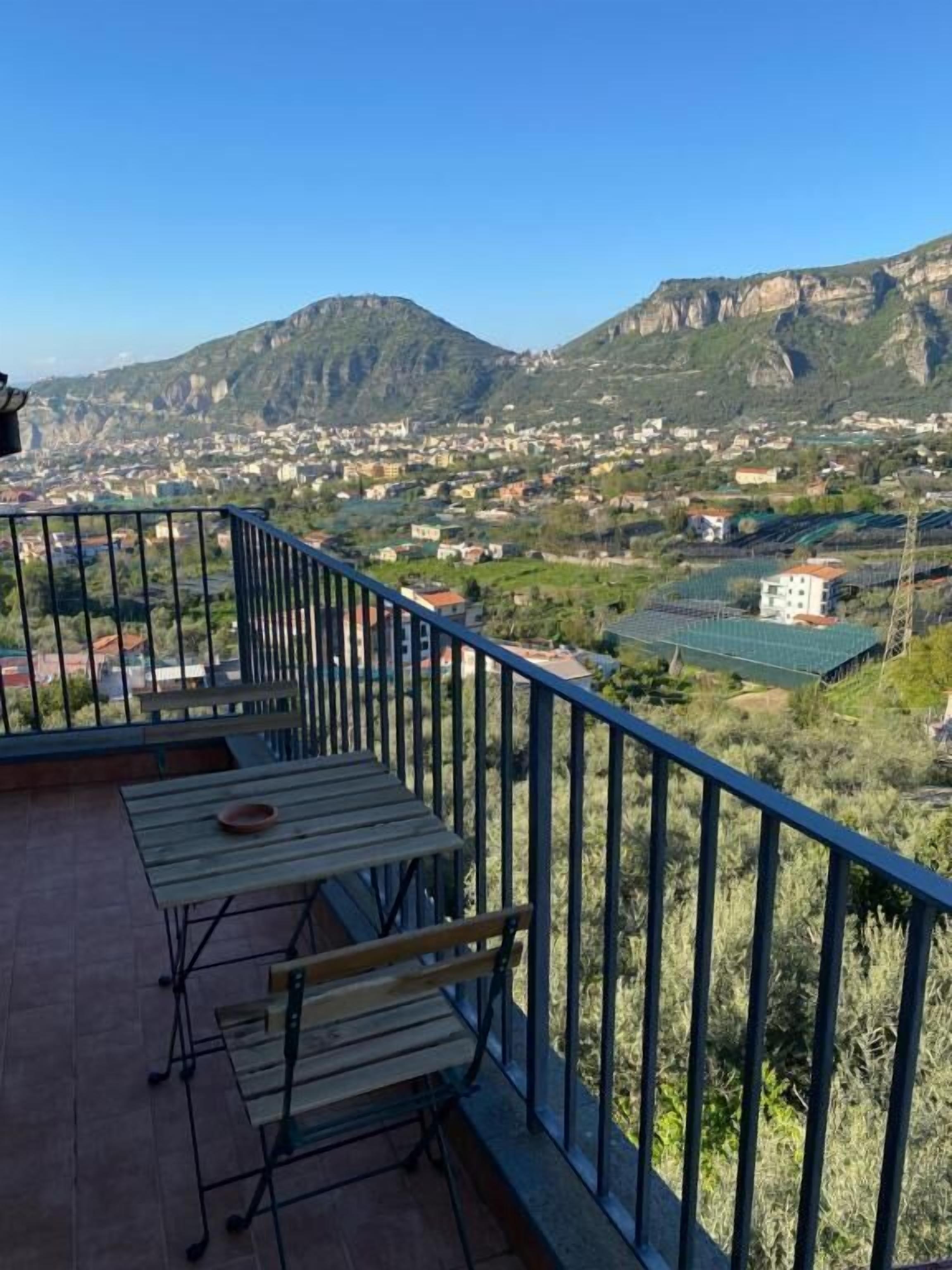 Un balcone con tavolo e panca, affacciato su un paesaggio montuoso con edifici.