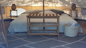 A tent with a bed, a hanging chair, a woven basket, and a metal table.