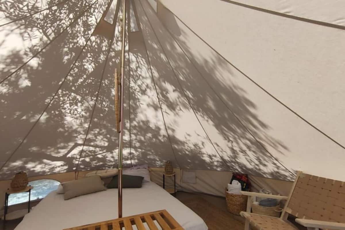 Una tienda de campaña con una cama, una mesa de madera, una silla y una mesita con una lámpara.