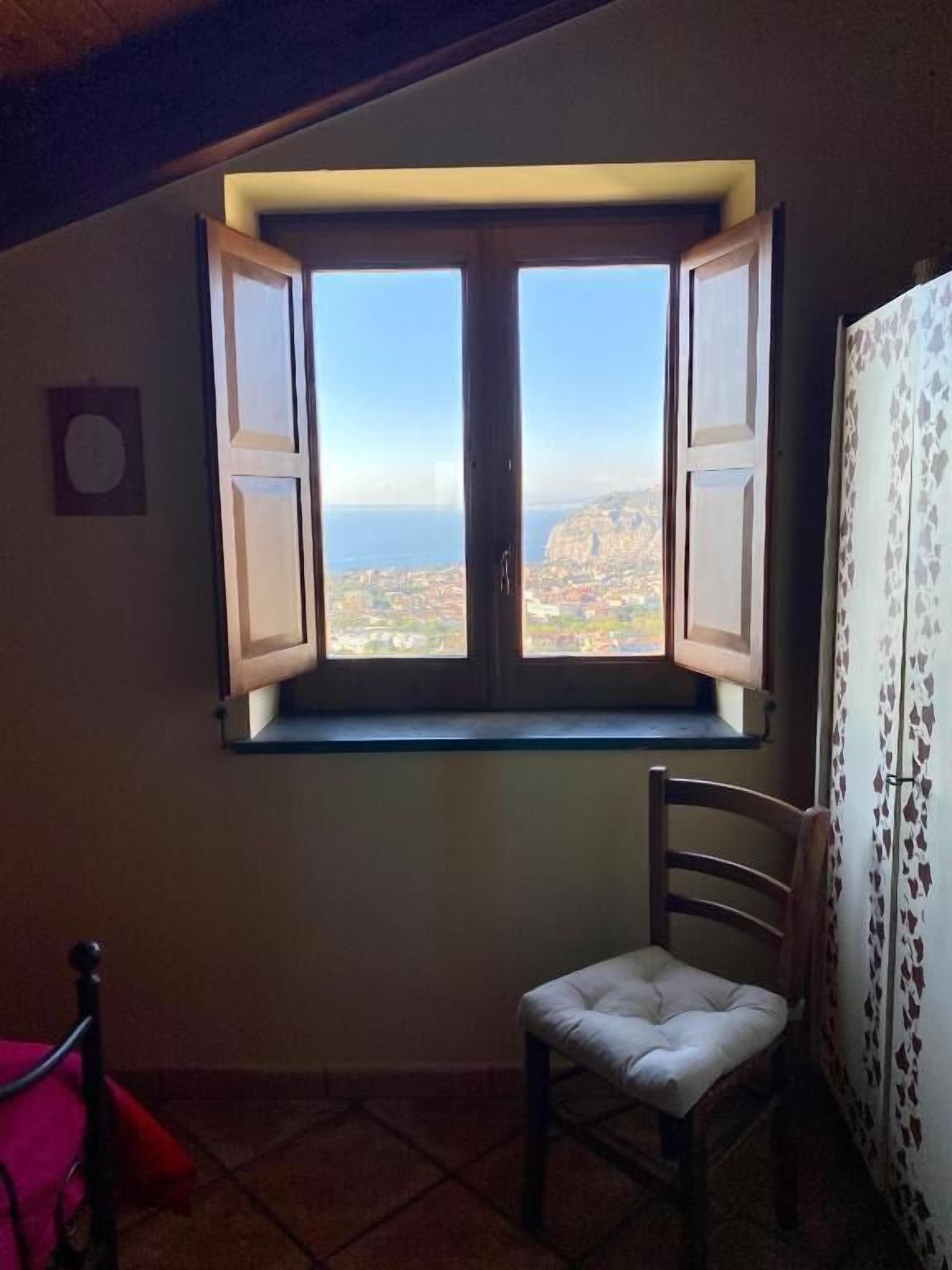 Ein Zimmer mit Fenster und Meerblick, ein Sessel und eine Wand mit Muster.