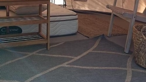 A tent interior with a mattress, a small table, and a woven basket.
