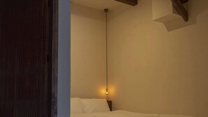 A bedroom with a single bed, a hanging light fixture, and a wooden ceiling beam.