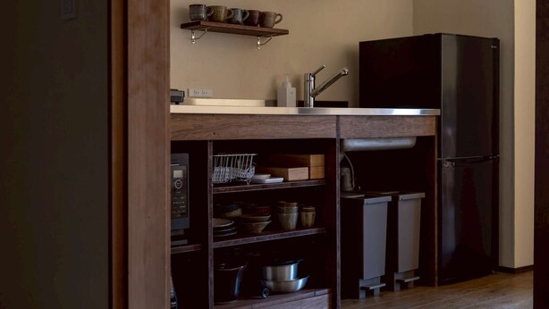 A kitchen with wooden shelves, a black refrigerator, and a coffee machine.