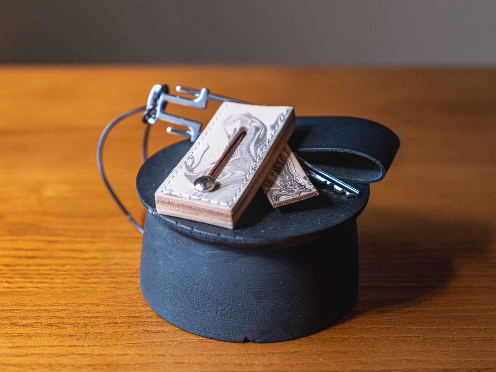 Een klein, donker object met een ronde vorm en een metalen clip aan de bovenkant, op een houten oppervlak geplaatst.