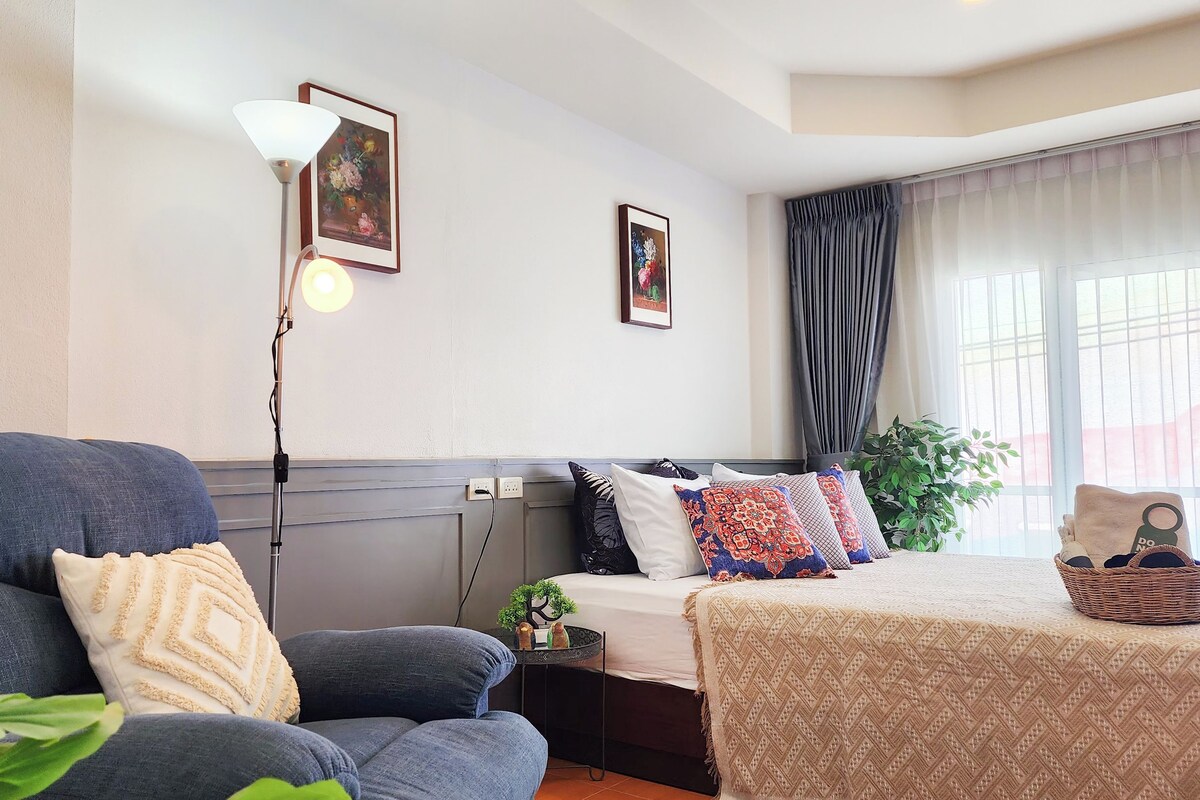 Una habitación luminosa con sofá, cama, lámpara y ventana con cortinas.