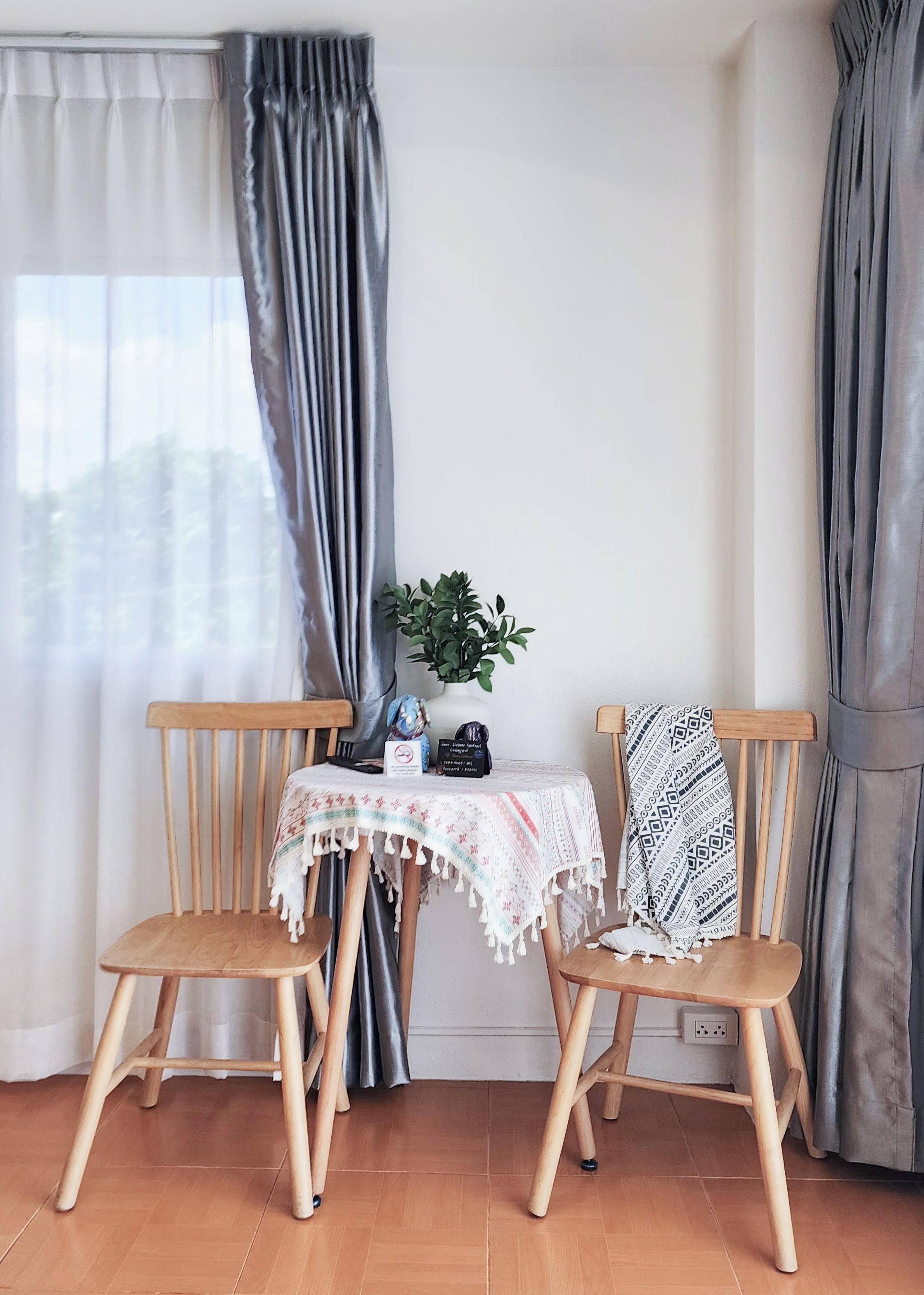 A room with two wooden chairs, a small table with a tablecloth, a potted plant, and a wall socket.