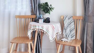Een kamer met twee houten stoelen, een tafeltje met tafelkleed, een kamerplant en een stopcontact.