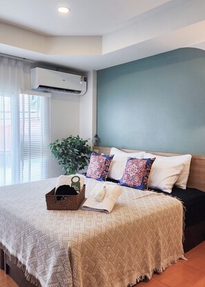 A hotel room with a bed, air conditioning unit, window with blinds, and a potted plant. - Baan Sinkaew Chiangmai (Chiang Mai)