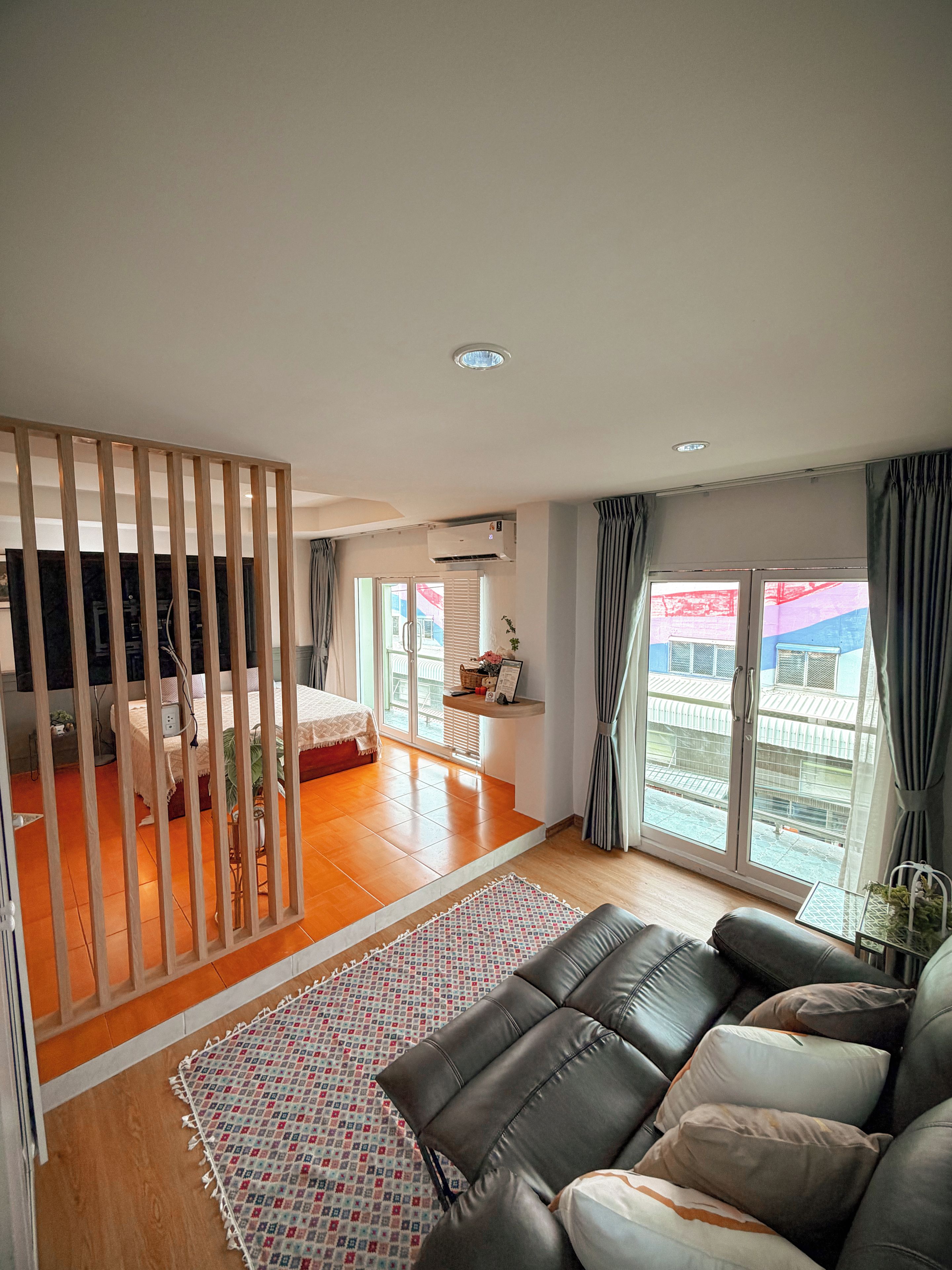 Un salon moderne avec un canapé, un tapis à motifs et une vue sur un balcon doté d’une balustrade.