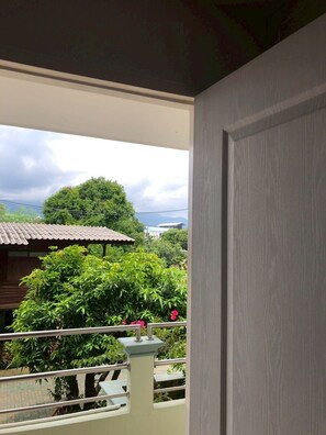 Un balcón con vistas a un paisaje verde, un edificio de techo de tejas y un cielo nublado.