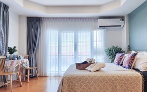 Een hotelkamer met een bed, een tafel met stoelen, een kamerplant en een airconditioning.