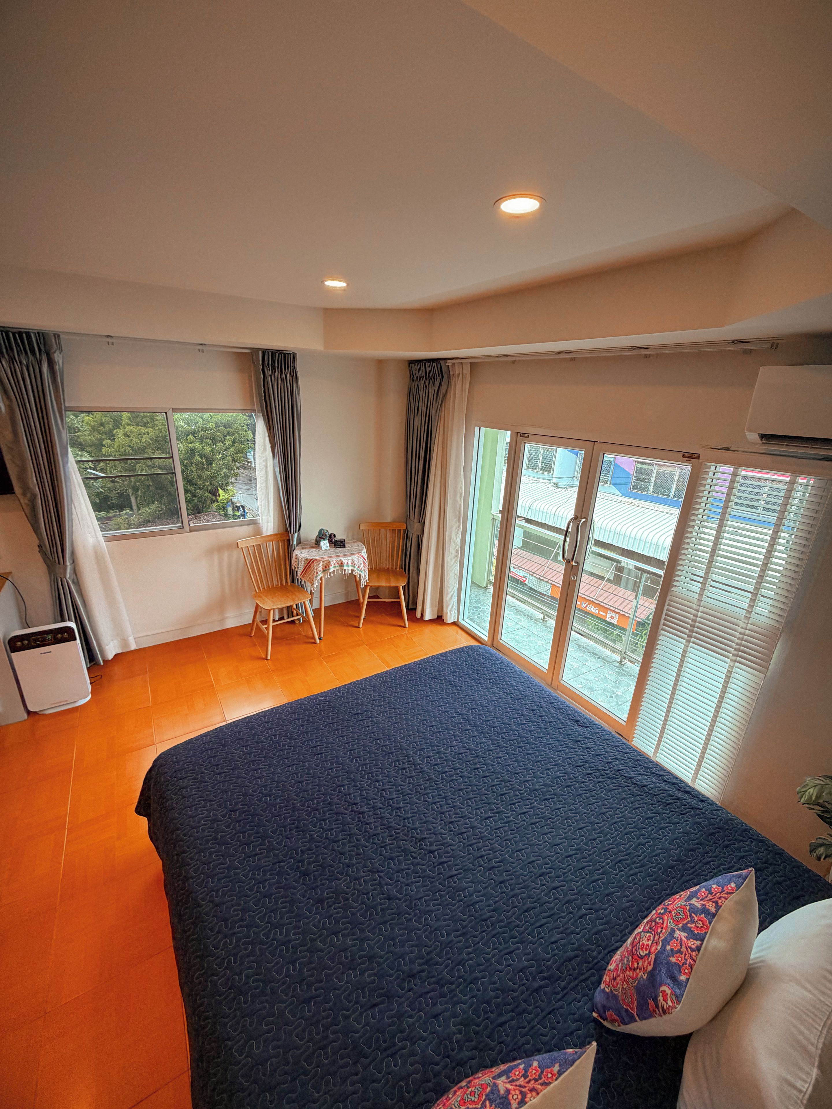 A hotel room with a large bed, a small table, chairs, and a view through the window.