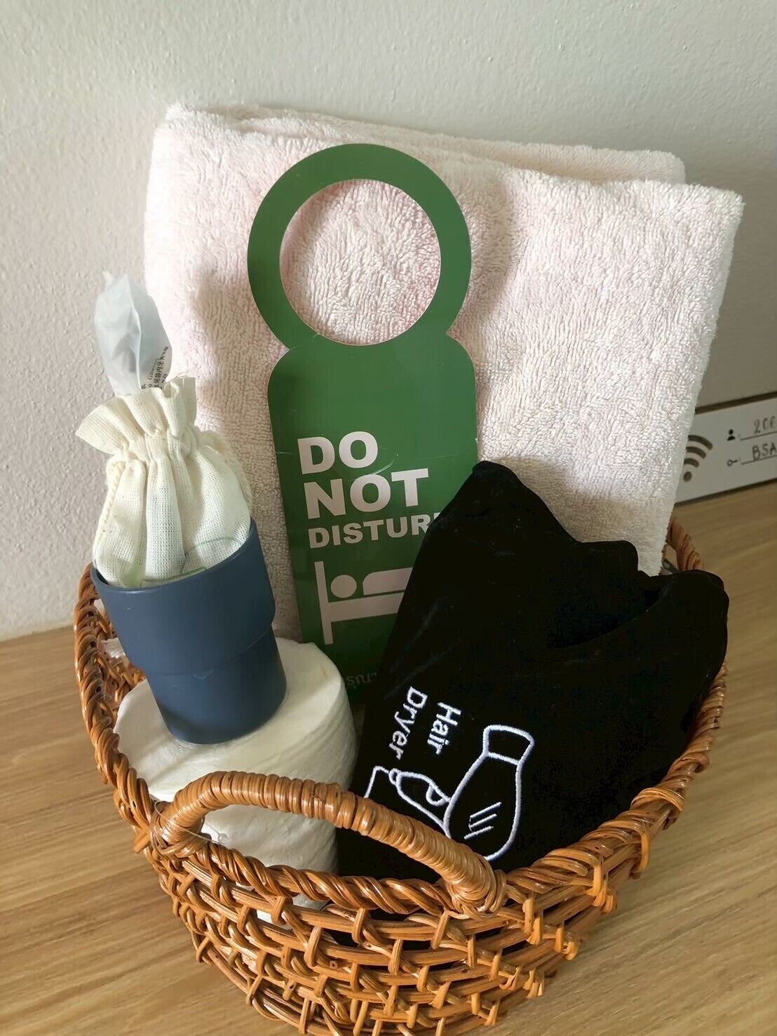 Una cesta de mimbre con una toalla blanca, un cartel verde que dice 'NO MOLESTAR', un secador de pelo negro y un paño blanco.