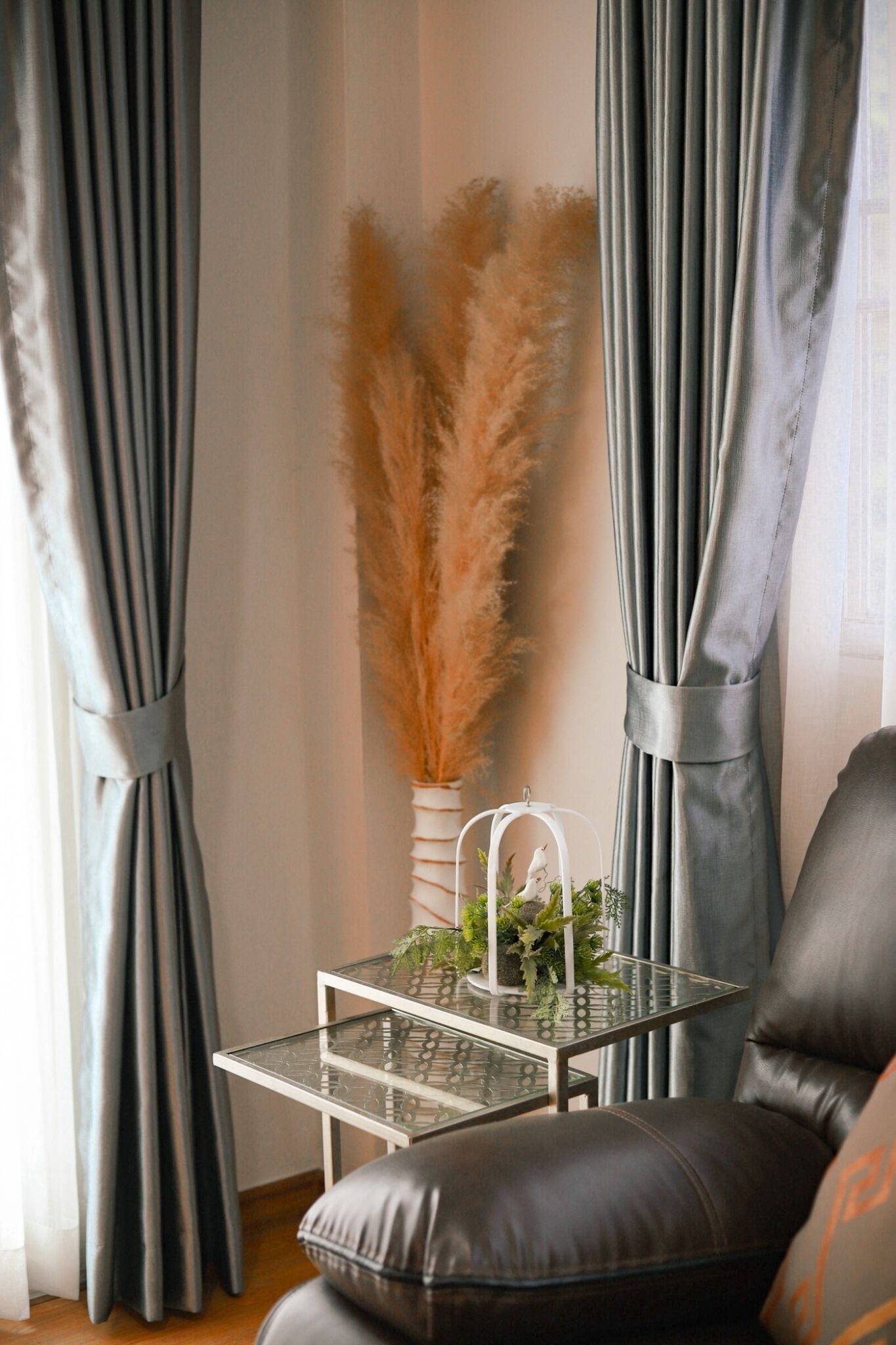 A room with a glass table, a leather chair, and grey curtains.