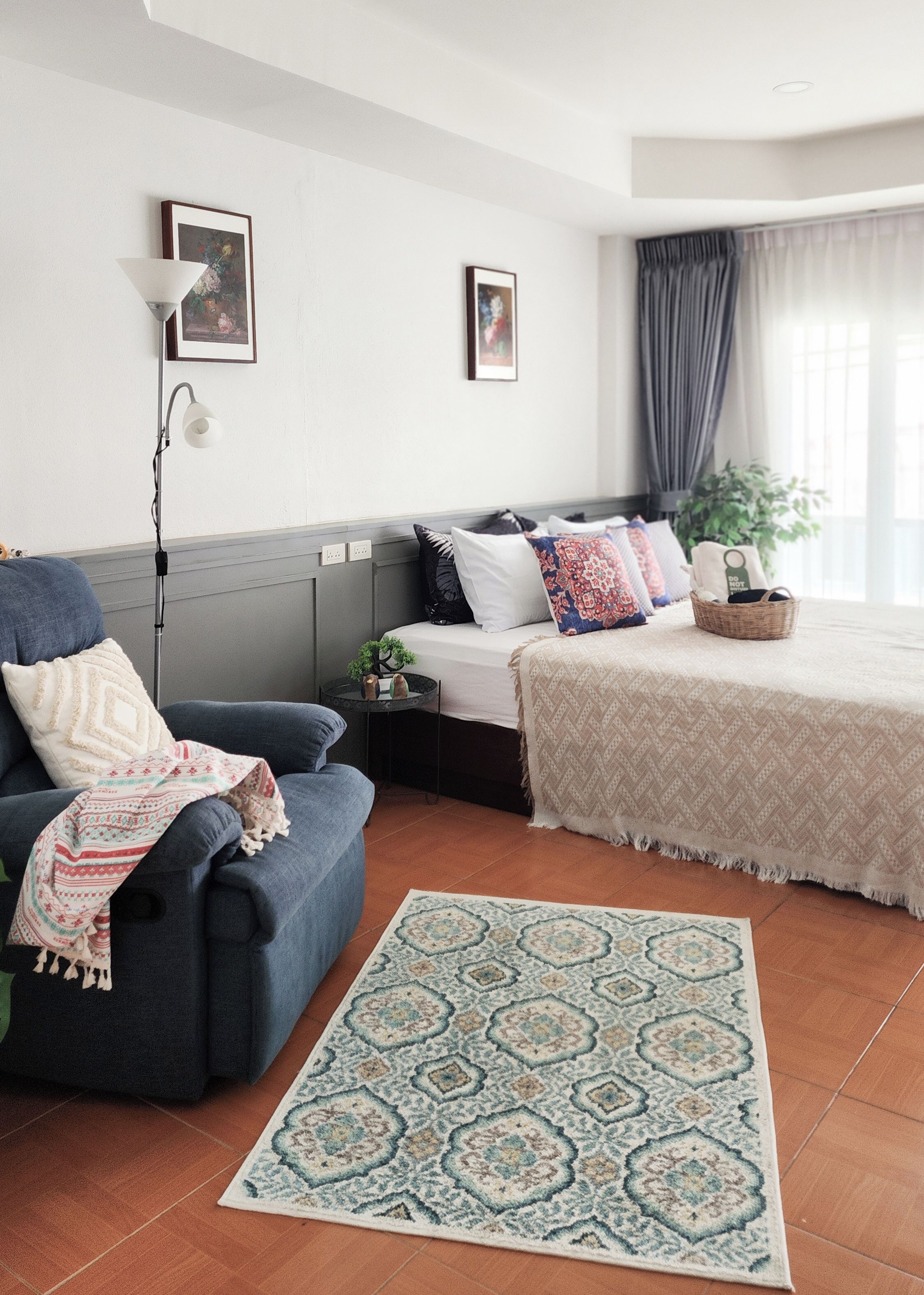 A modern bedroom with a bed, a sofa, a floor lamp, and a patterned rug.