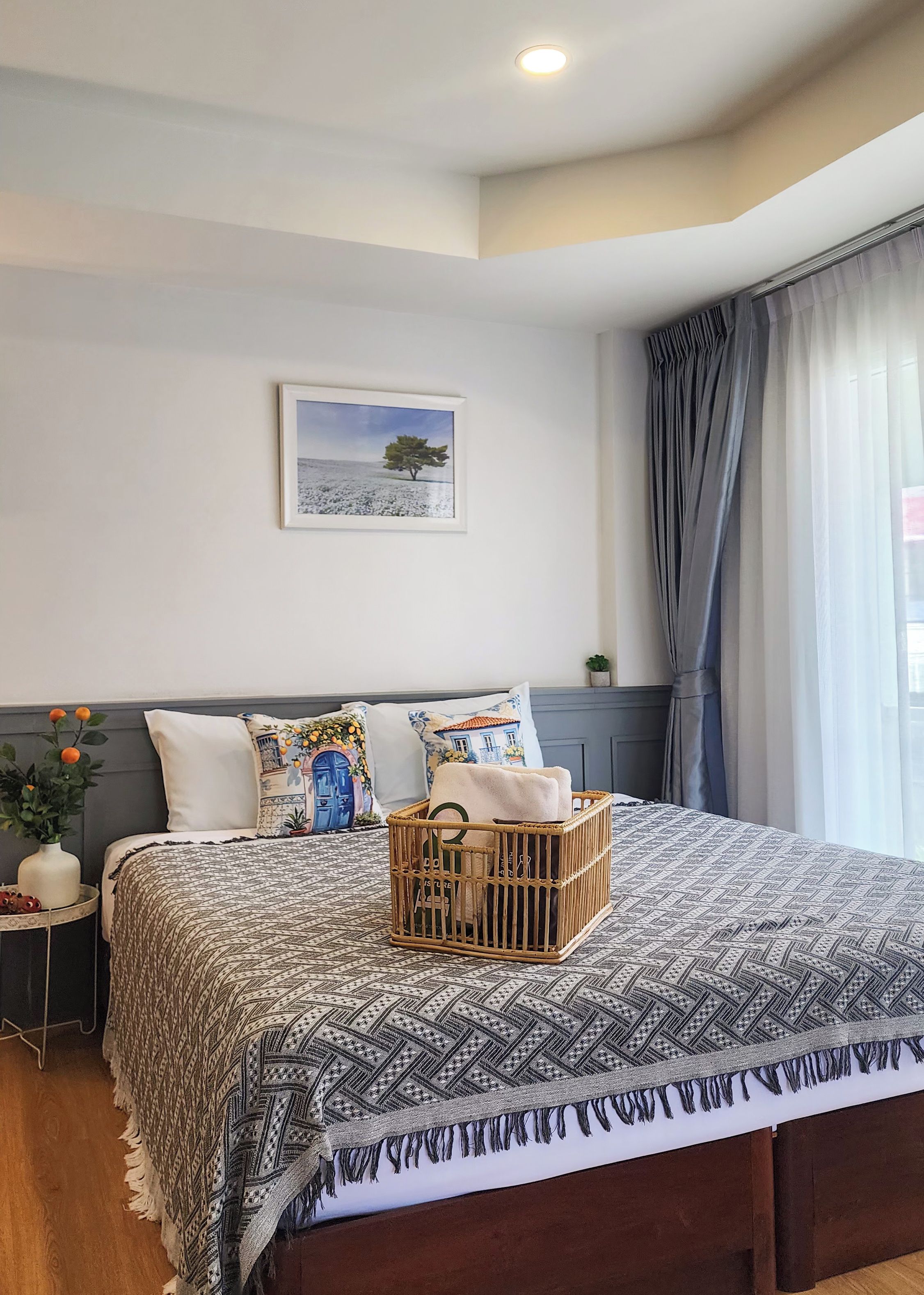 Cama bem arrumada com colcha estampada, um cesto decorativo sobre a cama e um quadro na parede.