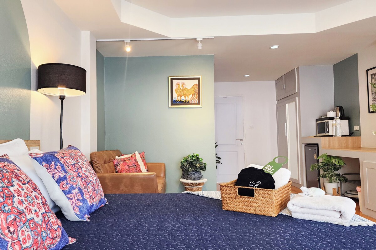 Una habitación de hotel con cama, sofá, lámpara, un cuadro, zona de cocina y baño.