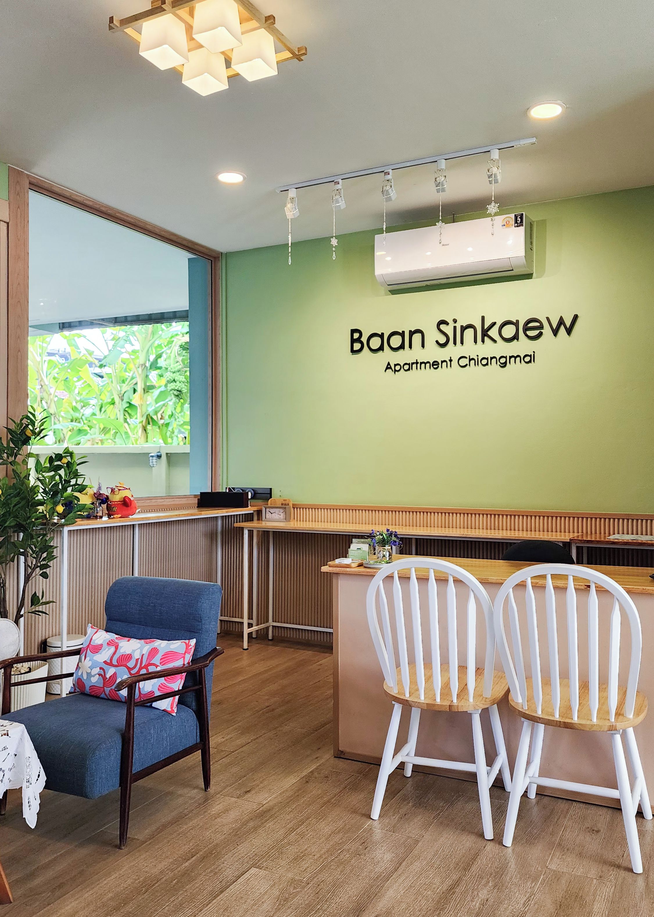 A reception area with a green wall, a reception desk, a clock, and a window with a view of greenery.