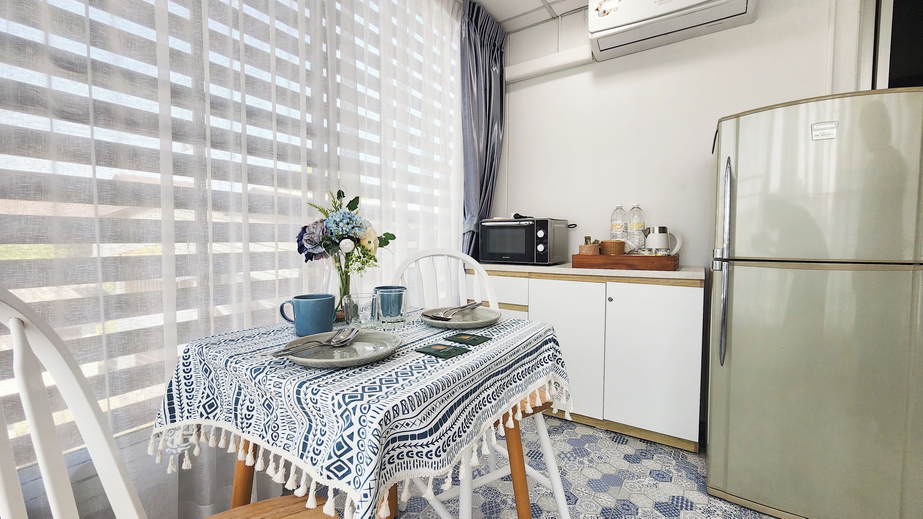 A small kitchenette with a refrigerator, microwave, and a dining area with a table set for two.