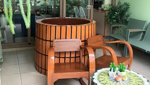Um espaço de lobby com uma mesa redonda de madeira, duas cadeiras, uma mesinha redonda com um toalha de renda e uma placa na parede indicando a área de lobby.