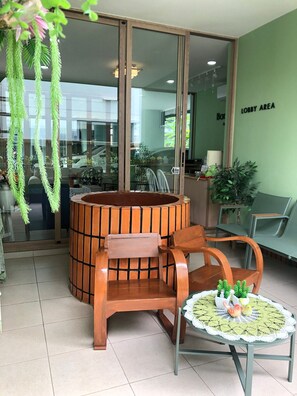 Un área de recepción con una mesa redonda de madera, dos sillas, una pequeña mesa redonda con un mantel y un letrero en la pared que indica el área de recepción.