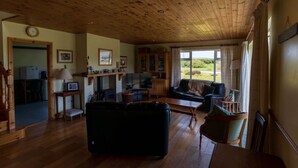 Ein geräumiges Wohnzimmer mit Holzboden, einer Couch, einem Fernseher und einem durch eine offene Tür einsehbaren Küchenbereich.
