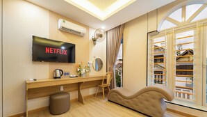 A modern hotel room with a flat-screen TV, wooden desk, comfortable seating, and a view through large windows. - Green Airport Hotel 2 (Ho Chi Minh City)