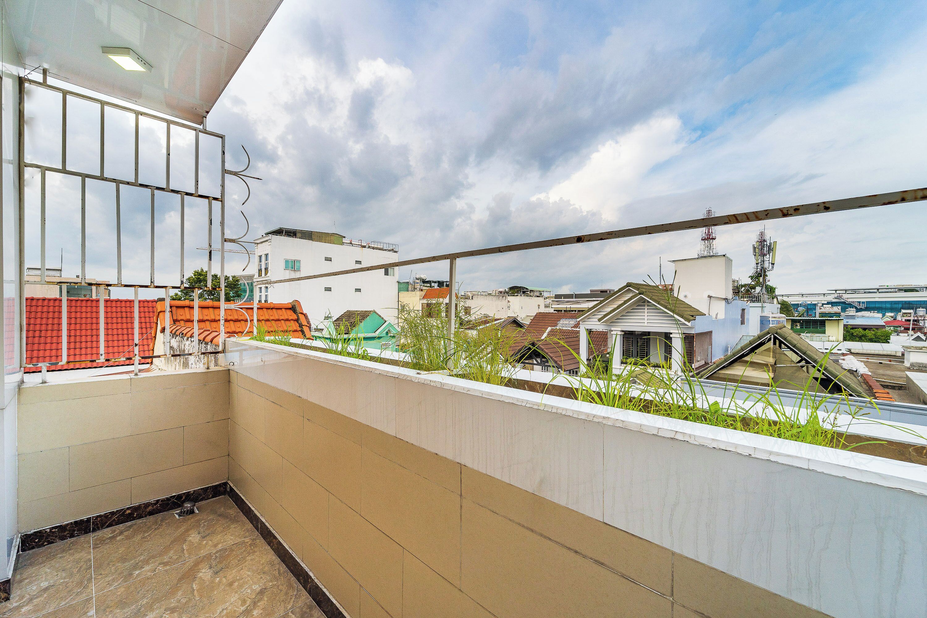 Ein Balkon mit Blick auf umliegende Gebäude, einem Metallgeländer und einem gefliesten Boden.
