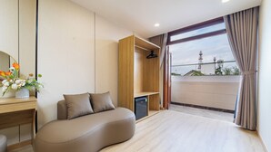 A modern bedroom with a curved sofa, a wooden wardrobe, and a view of the outside. - Green Airport Hotel 2 (Ho Chi Minh City)