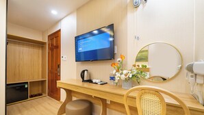 A hotel room with a wooden desk, a television mounted on the wall, a mirror, a hairdryer, and a small refrigerator. - Green Airport Hotel 2 (Ho Chi Minh City)