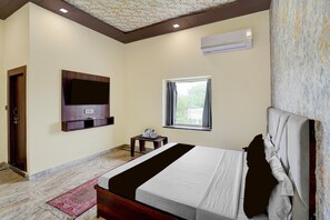 Une chambre d’hôtel équipée d’un lit, d’un téléviseur fixé au mur, d’une fenêtre avec des rideaux et d’un appareil de climatisation.
