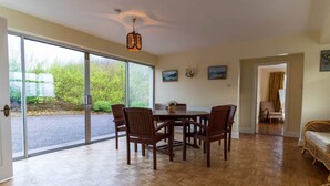Comedor con mesa y sillas, una araña y vistas a un área exterior a través de grandes puertas correderas.