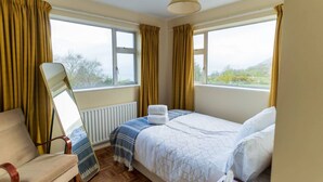 Un dormitorio con cama, una silla, un ventanal y un radiador.