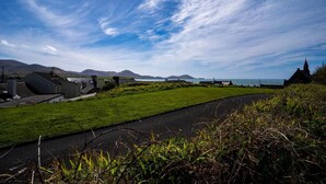A coastal landscape with a grassy area, a paved path, and buildings including a church. - Finbarr’s House - Waterville (Waterville)