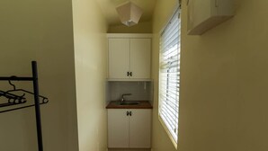 A narrow hallway leading to a small kitchen with a sink, cabinets, and a window with blinds. - Finbarr’s House - Waterville (Waterville)