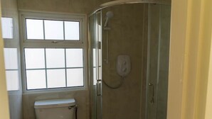 A compact bathroom with a toilet, a glass-enclosed shower, and a window providing natural light. - Finbarr’s House - Waterville (Waterville)