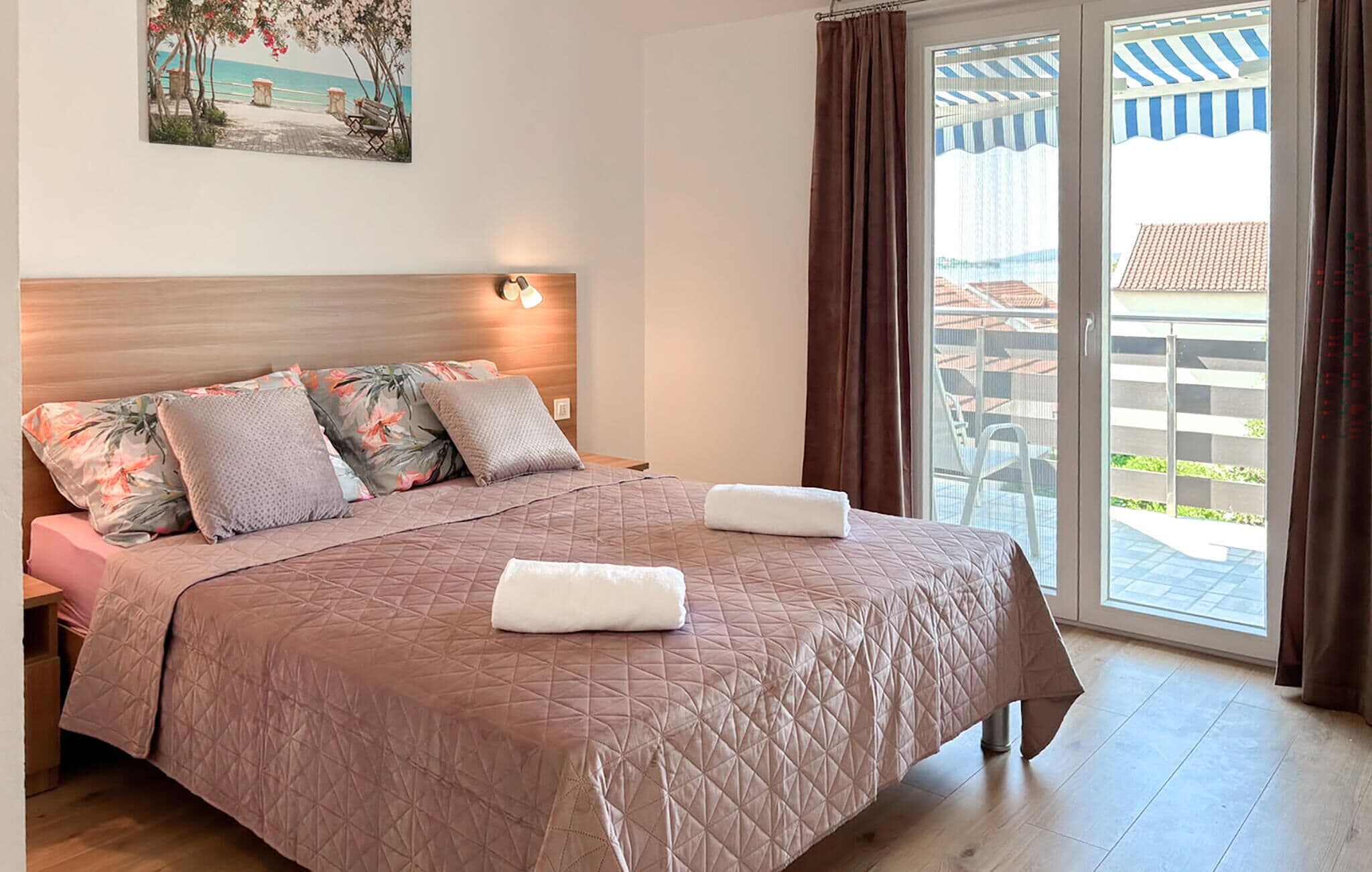 Ein Schlafzimmer mit Bett, Kissen, einem Kopfteil, einem Gemälde und Blick ins Freie.