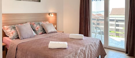 A bedroom with a bed, pillows, a headboard, a painting, and a view of the outside.