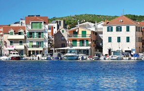 Un pueblo costero con edificios a lo largo del paseo marítimo, barcos amarrados y un cielo azul despejado.
